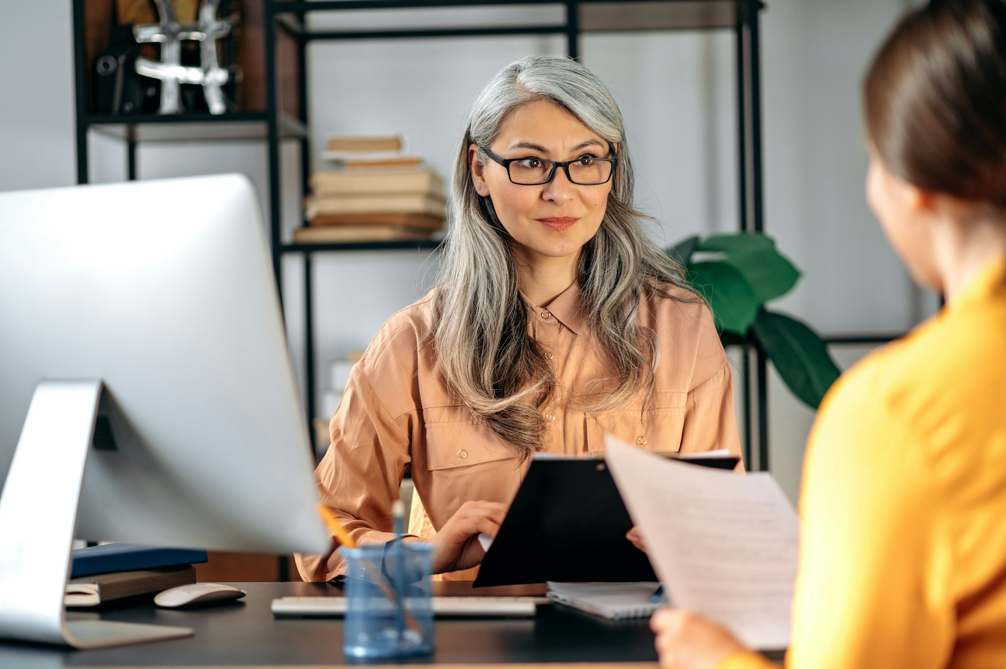 Gray-haired female HR manager with glasses, job candidate, resume.